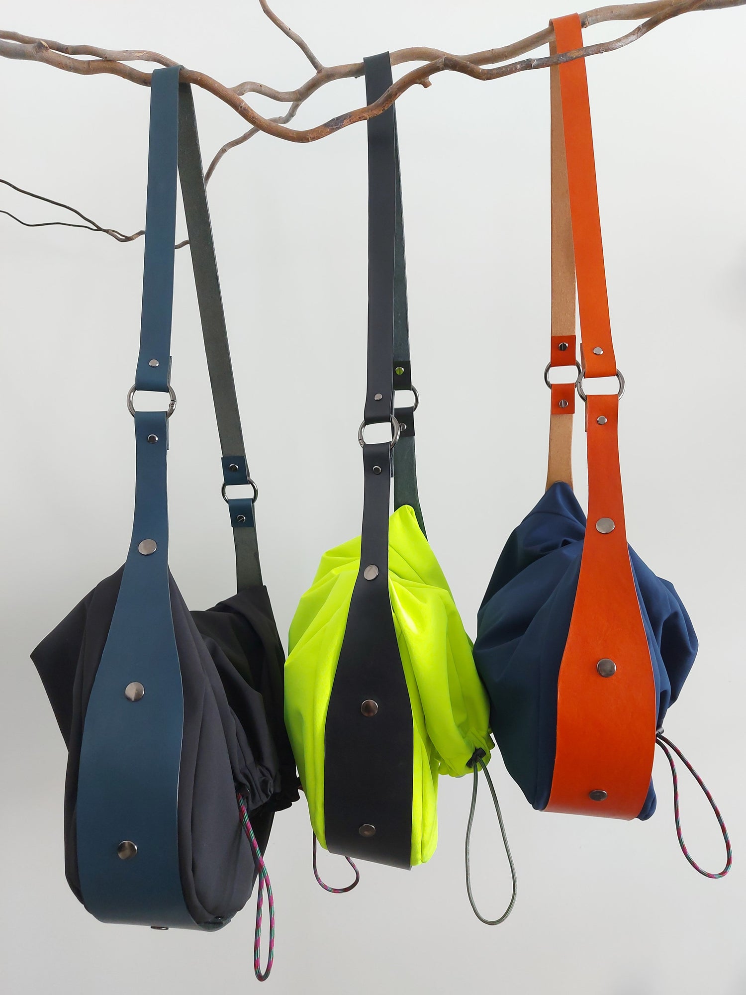 Three colorful bags hanging from a branch against a white background