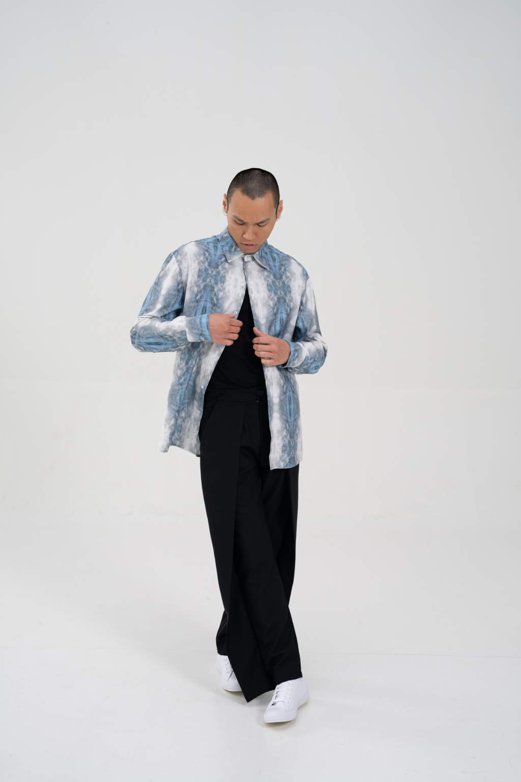 A man modeling a light blue and white marbled patterned jacket over a black shirt and black wide-leg trousers, standing against a seamless white studio background. Collaboration print 001 tailored shirt by September Archive. Captured by Paper Crane Creative.