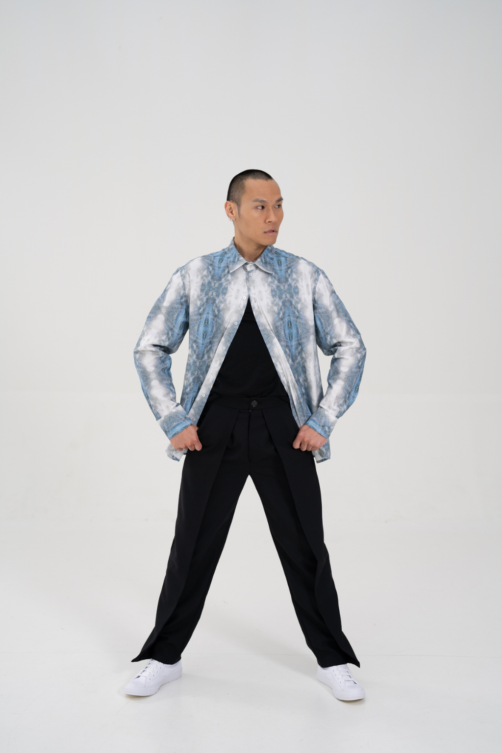 A man modeling a light blue and white patterned jacket over a black shirt and black trousers, standing against a plain light gray studio background. Collaboration print 001 tailored shirt by September Archive. Captured by Paper Crane Creative.