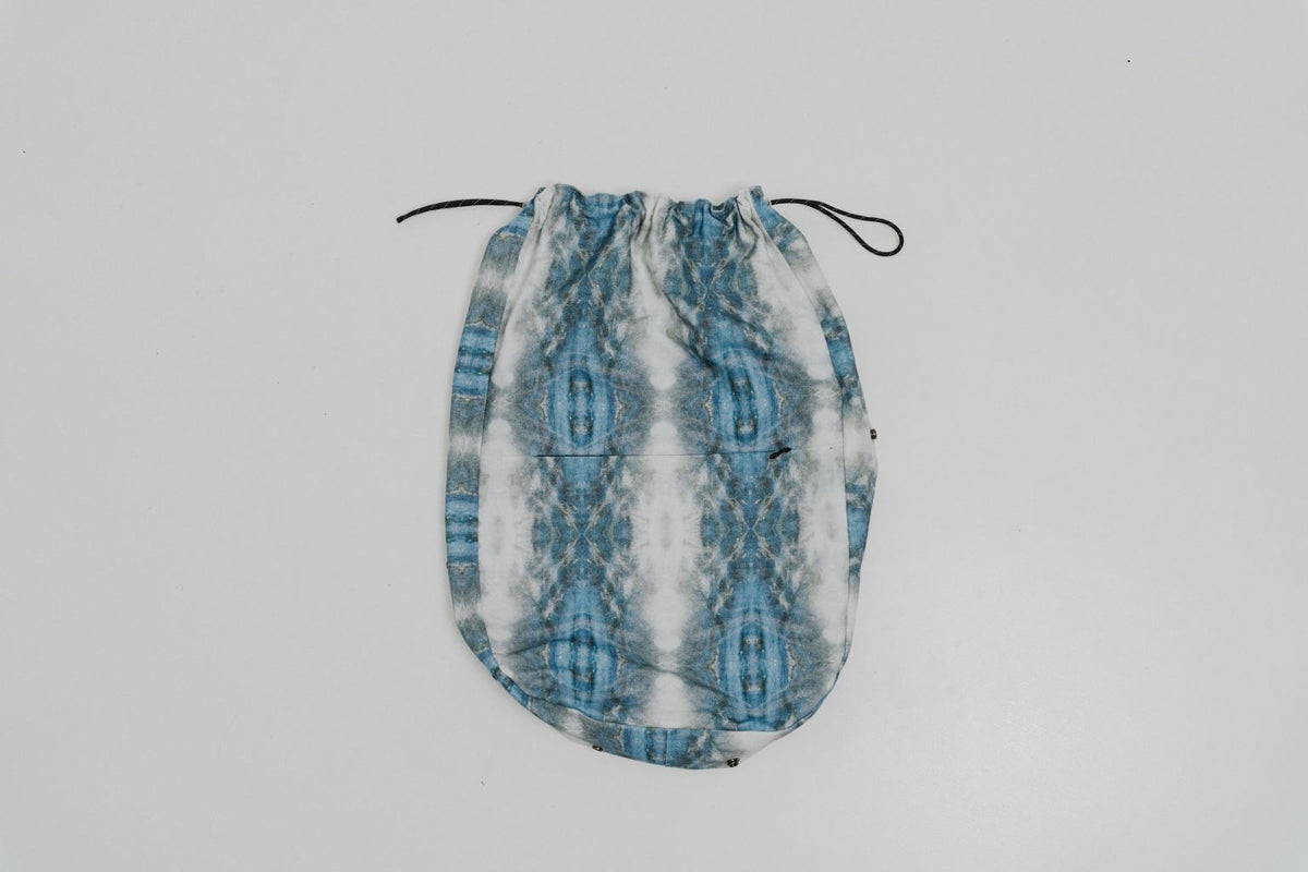 A drawstring pouch with a blue and white vertical ikat pattern, shown against a plain light gray background. Project collab #001: Carryall City Sling bag with collaborative all-over print by September Archive Apparel. Captured by Paper Crane Creative.