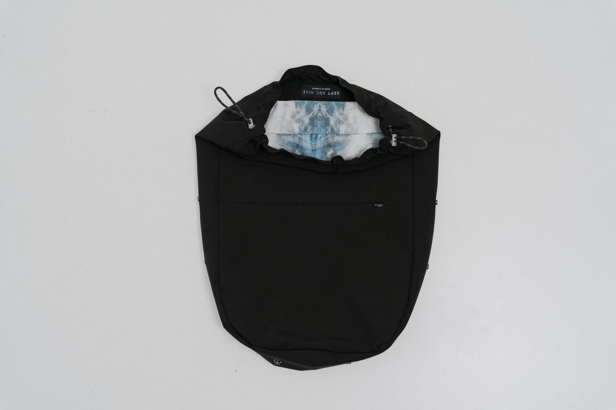 A black drawstring bag with a white and blue patterned face mask tucked inside, photographed from above on a light gray background. Project collab #001: Carryall City Sling bag with collaborative lining print by September Archive Apparel. Captured by Paper Crane Creative.