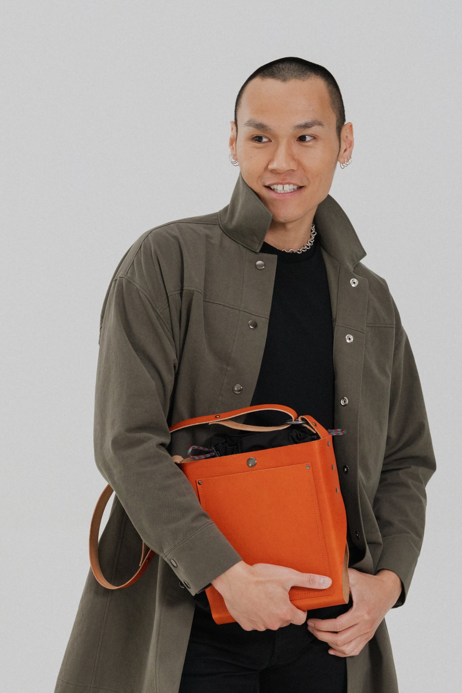 Man holding an orange leather bag by September Archive while wearing a dark olive Atelier Jacket.