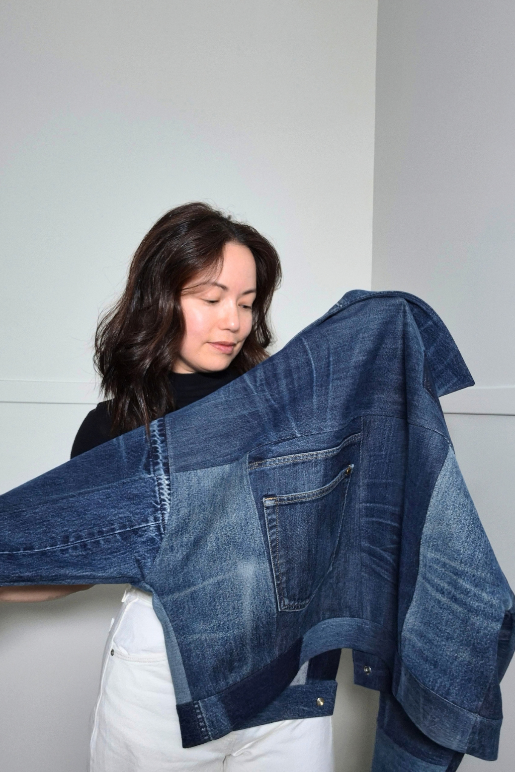 A woman holding up a cropped, oversized denim jacket made from multiple blue denim jeans, showing the layered patchwork construction and front pocket.
Upcycled denim jacket by September Archive Apparel. Canadian made denim jacket. One of a kind cropped denim jacket made in Vancouver, Canada. Photographed by Sheila Wong.