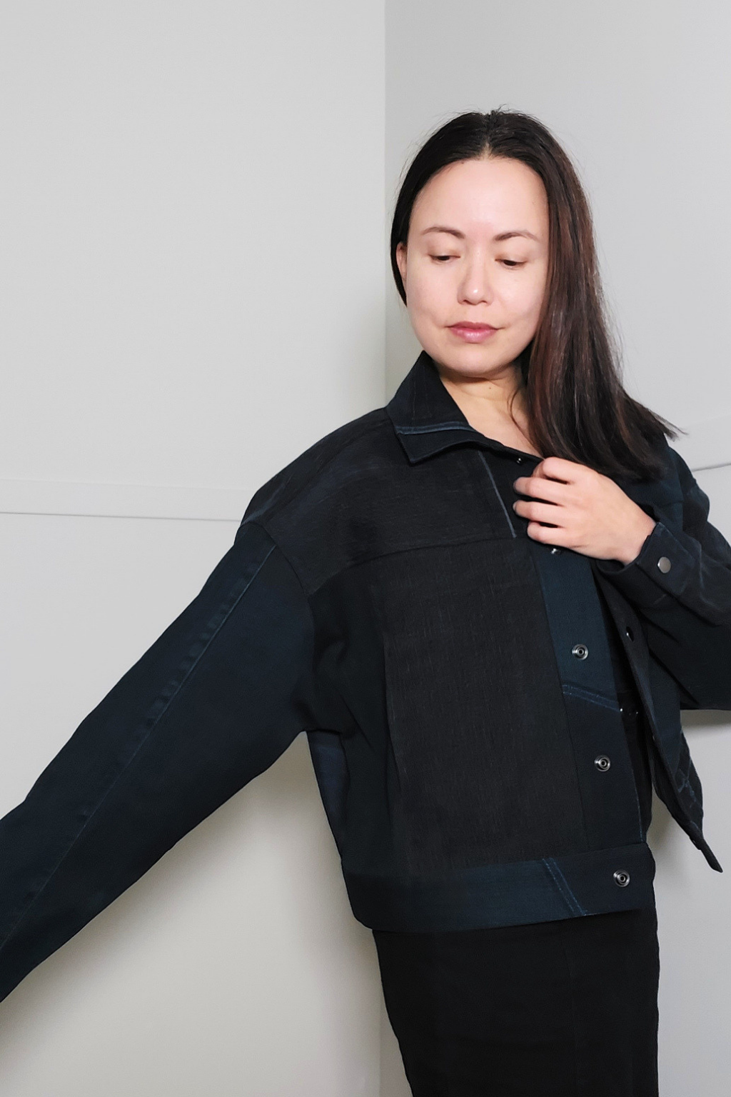 A woman wearing a dark navy blue cropped jacket with contrasting textured panels, posed against a minimalist light gray background. Upcycled denim jacket by September Archive. Photographed by Sheila Wong.