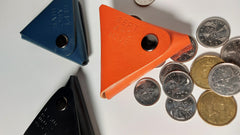 Three triangular leather coin pouches on a white surface with coins around them.